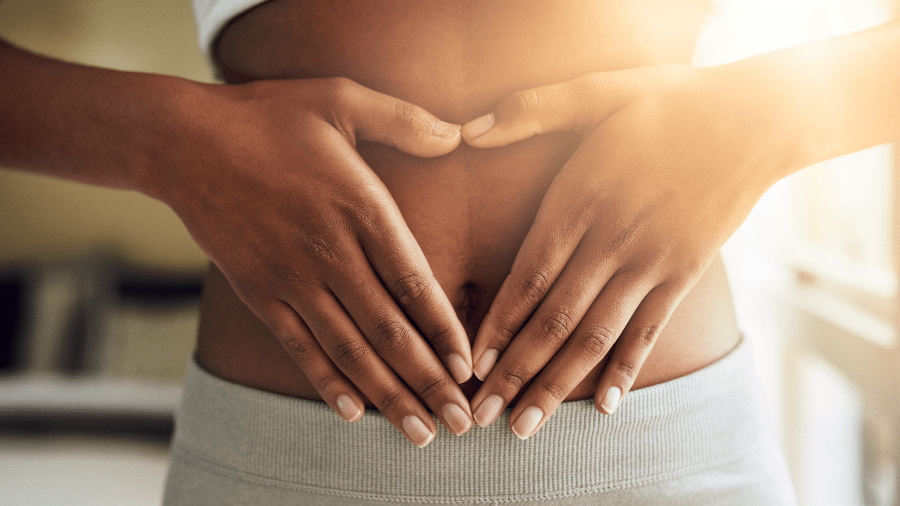 Woman is making a heart around her stomach using her hands 