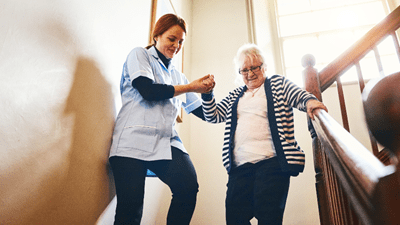 A home health care professional helping her patient down the stairs.