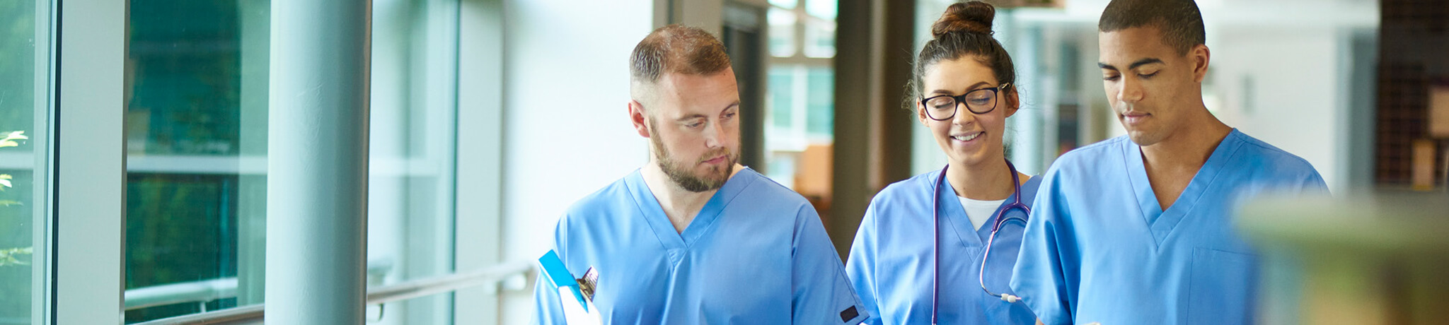 three members of medical staff walking through hospital with clipboards