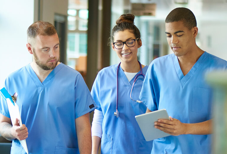 three members of medical staff walking through hospital with clipboards